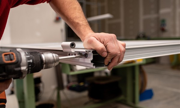 Technician assembling an aluminium frame profile and operating hardware in a workshop