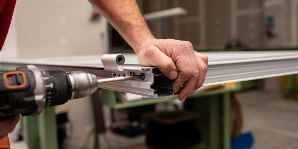 Technician assembling an aluminium frame profile and operating hardware in a workshop